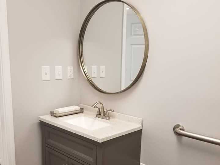 Small bathroom with round mirror, gray vanity, and towel on counter.