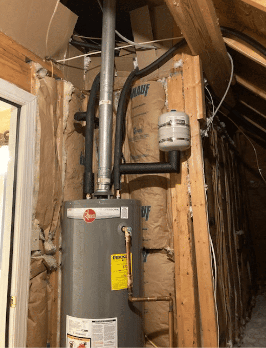 Basement water heater with insulation and pipes in an unfinished room.